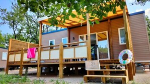 A wooden deck with a bench, a small table, and a colorful inflatable ring. - ZEcamping 3 étoiles dog friendly mobil-home TV LV clim 34m2 8 pers (Bauduen)