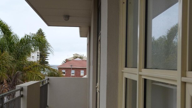 Un balcon étroit doté d’une rambarde en métal, d’un sol en béton et offrant une vue sur un bâtiment aux toits rouges en arrière-plan.