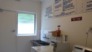 Une buanderie équipée d’un lave-linge, d’un sèche-linge et d’un évier. Des panneaux explicatifs sont affichés au mur.