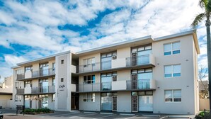 Un immeuble résidentiel à plusieurs étages, doté de balcons, d’un parking et surplombant un ciel dégagé.