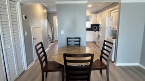 Un comedor con una mesa redonda y cuatro sillas, una cocina al fondo y un pasillo que lleva a una puerta.
