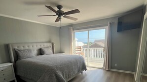 Un dormitorio con cama, mesita de noche, ventilador de techo y vistas al exterior.