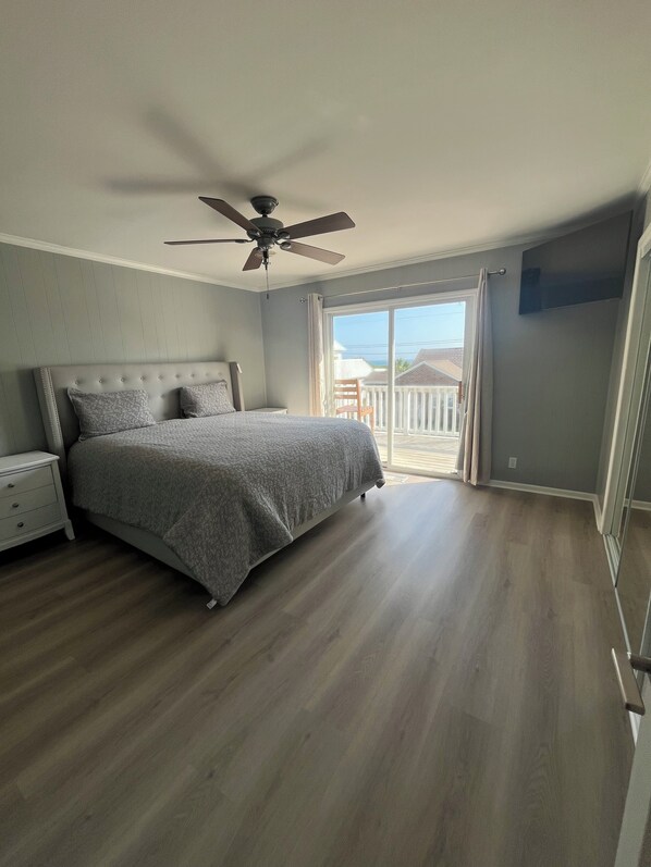 Un dormitorio con cama, mesita de noche, ventilador de techo y vistas al exterior.
