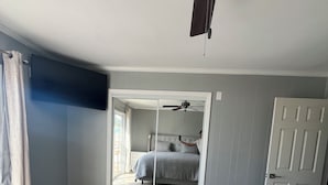 Un dormitorio con cama, ventilador de techo, puerta y un espejo grande.