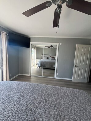 Une chambre à coucher avec un lit, un ventilateur de plafond, une porte et un grand miroir.