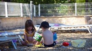 Two children playing with toys on a gravel surface near a white fence. - ZEcamping 3* piscine animaux acceptés locatif TV clim 15m2 2 pers (Mézel)