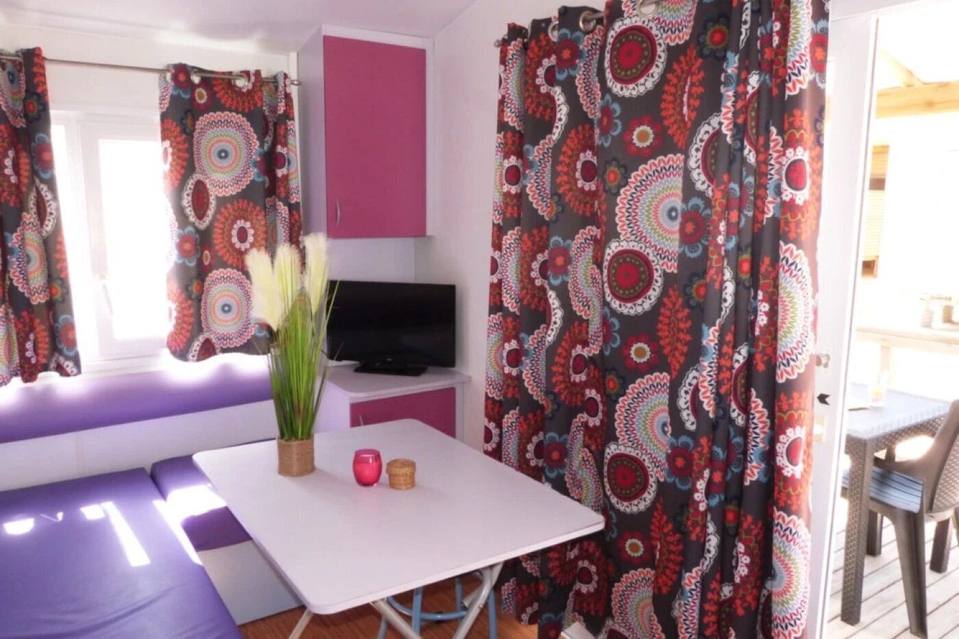 Ein Zimmer mit einem weißen Tisch, einer rosa Kommode, einem Fernseher und einem Vorhang mit Muster.