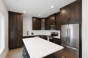 Una cocina moderna con armarios de madera oscura, electrodomésticos de acero inoxidable y encimera blanca.