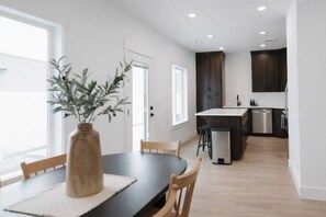 Una cocina moderna con gabinetes oscuros, una isla central y una zona de comedor con mesa y sillas.