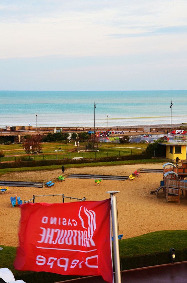 Blick auf einen Strand mit einer Flagge, einem Sandbereich und einem Gebäude im Hintergrund.