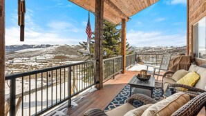 A covered outdoor area with a view of a snowy landscape, furnished with a sofa, chairs, and a table.
