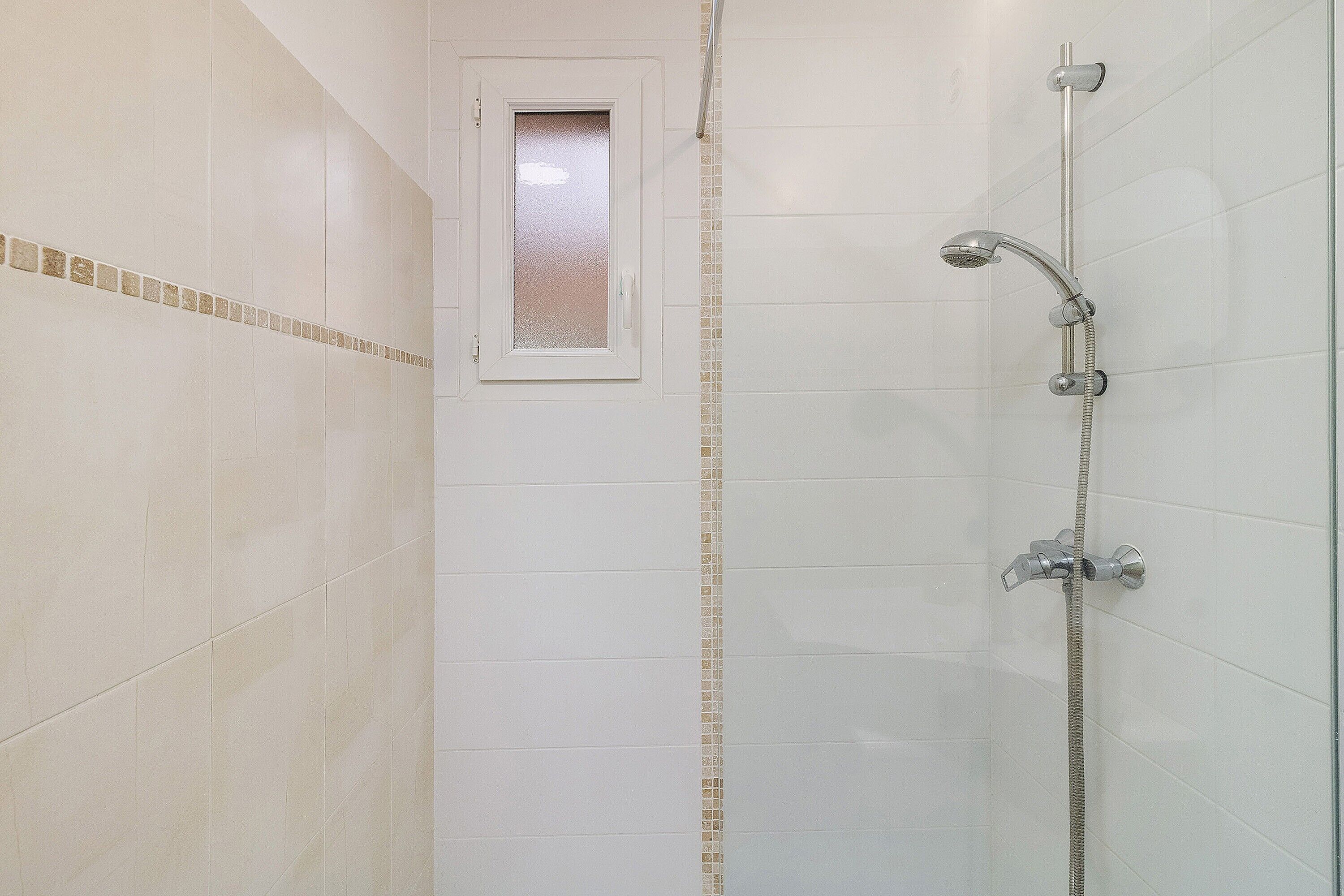 Une salle de bain avec des carreaux blancs, une douche et une petite fenêtre.