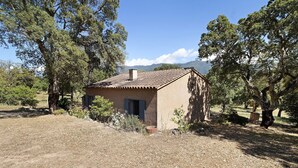 Una casa rustica con tetto in tegole, circondata da alberi e un cielo sereno.