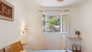 Una camera da letto con un letto, una finestra con tende, una lampada sul comodino, un tavolino e una mensola a muro.