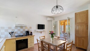 Una cucina compatta con zona pranzo, una TV fissata al muro e vista attraverso una porta aperta.