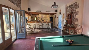 Ein Billardtisch mit Queue, ein Barbereich mit Hockern und ein Essbereich mit Stühlen.