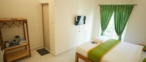 Quarto de hotel com cama, TV fixada na parede, guarda-roupa de madeira e cortina verde.