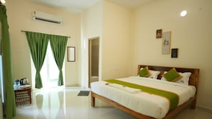 A hotel room with a large bed, a small table with a kettle, and a shower area. - Green Resort Pondicherry (Vanur)