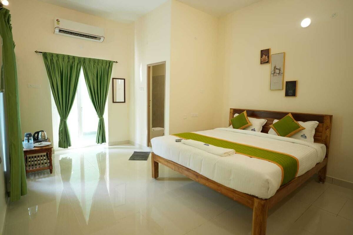 A hotel room with a large bed, a small table with a kettle, and a shower area.
