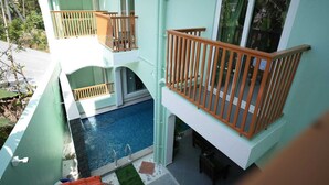 A two-story building with a swimming pool on the ground floor, wooden railings on balconies, and a view of palm trees. - Green Resort Pondicherry (Vanur)
