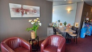 A hotel room with leather chairs, a small table, a vase with flowers, a painting on the wall, a dining area with chairs and a table, and a vending machine. - Hotel D Angleterre (Les Sables-d'Olonne)
