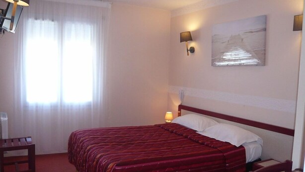 A hotel room with a large bed, a bedside table, a chair, a lamp, and a painting on the wall. - Hotel D Angleterre (Les Sables-d'Olonne)
