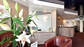 A modern living room with a leather sofa, a large potted plant, and a kitchen area in the background. - Hotel D Angleterre (Les Sables-d'Olonne)
