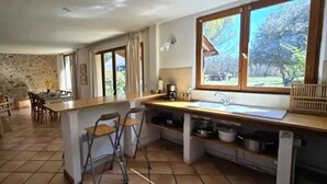 A kitchen with a stone wall, a dining area with chairs, a bar counter, and a large window with a view. - ZEcamping 3* piscine pet friendly locatif 90m2 6 pers (Quinson)