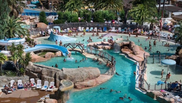 Una grande piscina esterna con diverse attrazioni acquatiche, tra cui scivoli e formazioni rocciose.