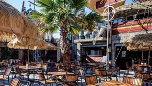 Un caffè all'aperto con ombrelloni di paglia, tavoli e sedie in legno.