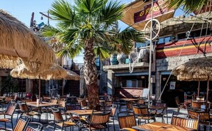 An outdoor cafe with thatched umbrellas, wooden tables, and chairs. - ZEcamping 4* animé 1km plage espace aquatique locatif TV LV clim 36m2 (Agde)