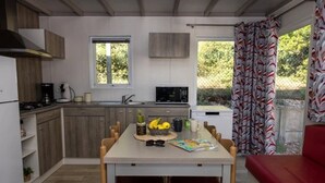 A compact kitchen with wooden cabinets, a dining table with chairs, and a red sofa. - ZEcamping 4* familial 1km plage piscine couverte jacuzzi chalet TV LV (Saint-Jean-de-Monts)