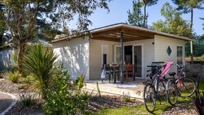 A single-story house with a patio, a covered seating area, and a bicycle parked outside. - ZEcamping 4* familial 1km plage piscine couverte jacuzzi chalet TV LV (Saint-Jean-de-Monts)