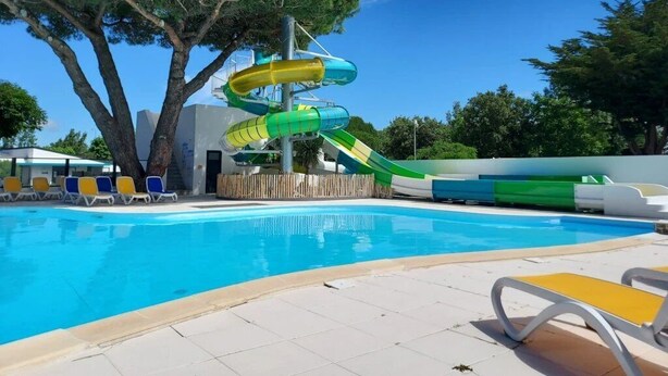 A swimming pool with a water slide, lounge chairs, and a tree. - ZEcamping 4* familial 1km plage piscine couverte jacuzzi chalet TV LV (Saint-Jean-de-Monts)