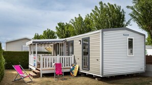 Ein Wohnwagen mit überdachter Veranda, einer kleinen Terrasse und einer Eingangstür.
