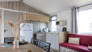Eine kleine Küche mit Kühlschrank, Mikrowelle und Gasherd. Ein Esstisch mit Stühlen und ein rotes Sofa mit Kissen sind ebenfalls vorhanden.
