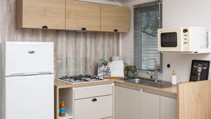 Eine kleine Küche mit einem weißen Kühlschrank, einem Gasherd, Holzschränken, einer Mikrowelle und einem Fenster mit Jalousien.