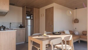A modern kitchen with wooden cabinets, a stainless steel refrigerator, and a dining area with a wooden table and chairs. - ZEcamping 4* piscine couverte locatif 4 pers (Pressignac)