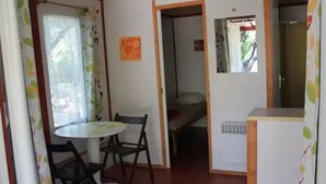 Ett litet rum med ett matbord och stolar, ett litet pentry och en säng i bakgrunden.