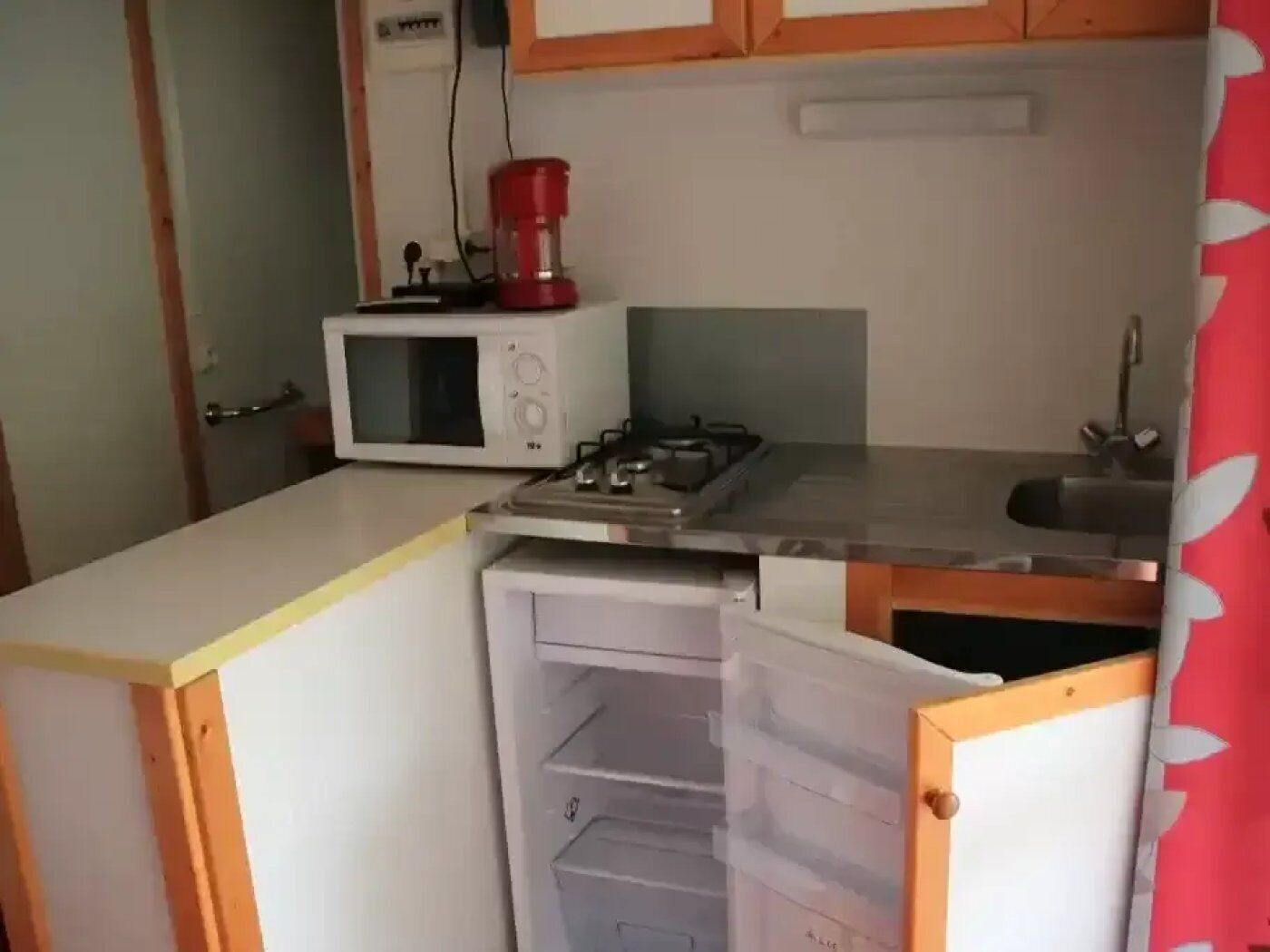 Pieni, käytännöllinen keittiö, jossa on mikroaaltouuni, punainen kahvinkeitin ja liesi.
