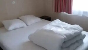 Ein ordentlich bezogenes Bett mit Kissen, einem Nachttisch und einem Fenster mit Vorhängen.
