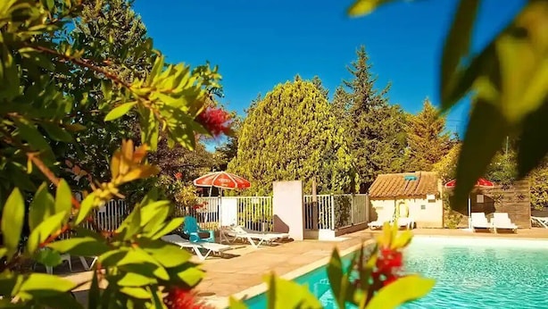 A swimming pool with lounge chairs and a red umbrella, surrounded by greenery and trees. - ZEcamping 3* pataugeoire piscine dog friendly mobil-home 22m2 3 pers (Junas)