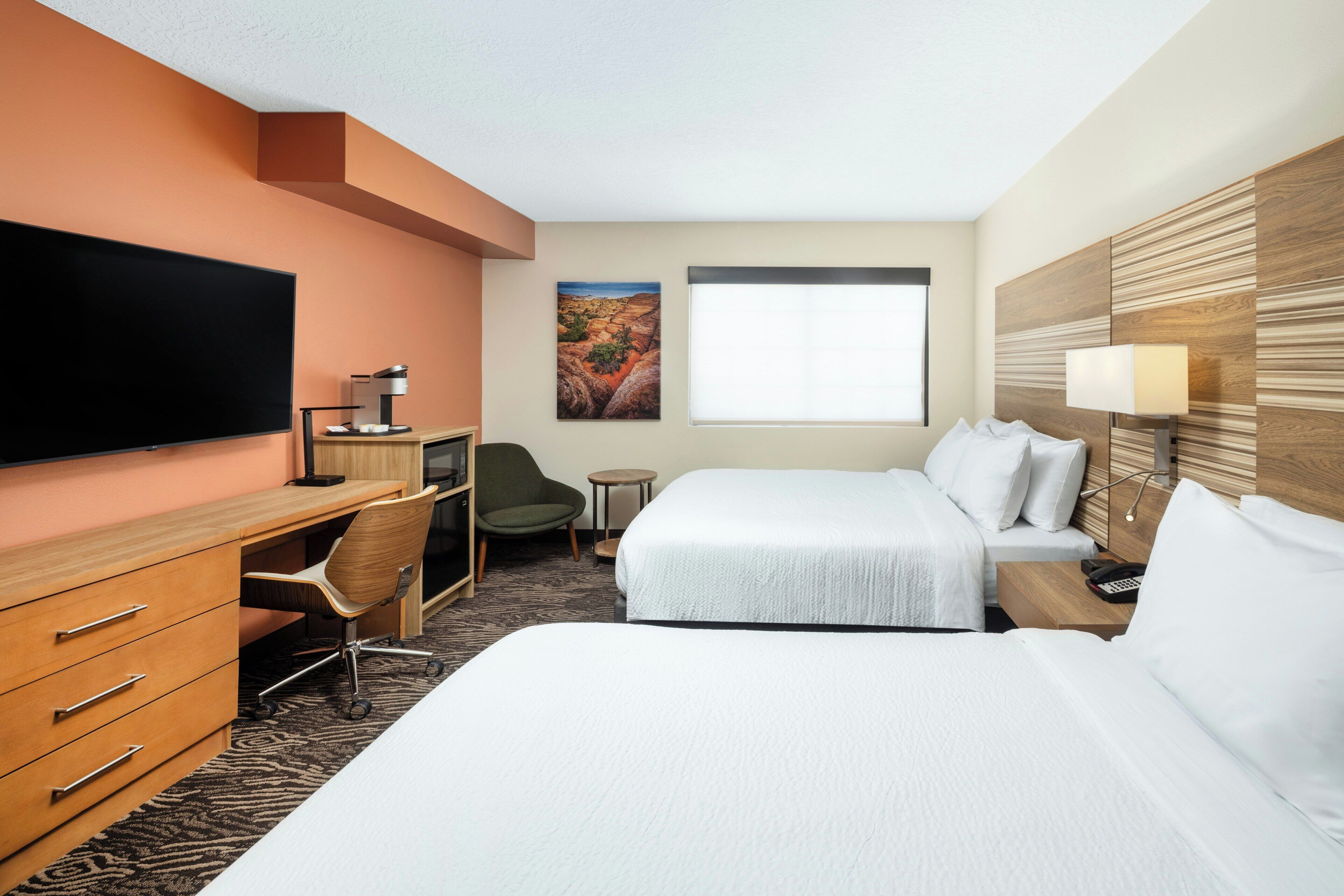 Hotelkamer met een flatscreen televisie, een bureau met stoel, twee bedden, een klein rond tafeltje en een schilderij aan de muur.