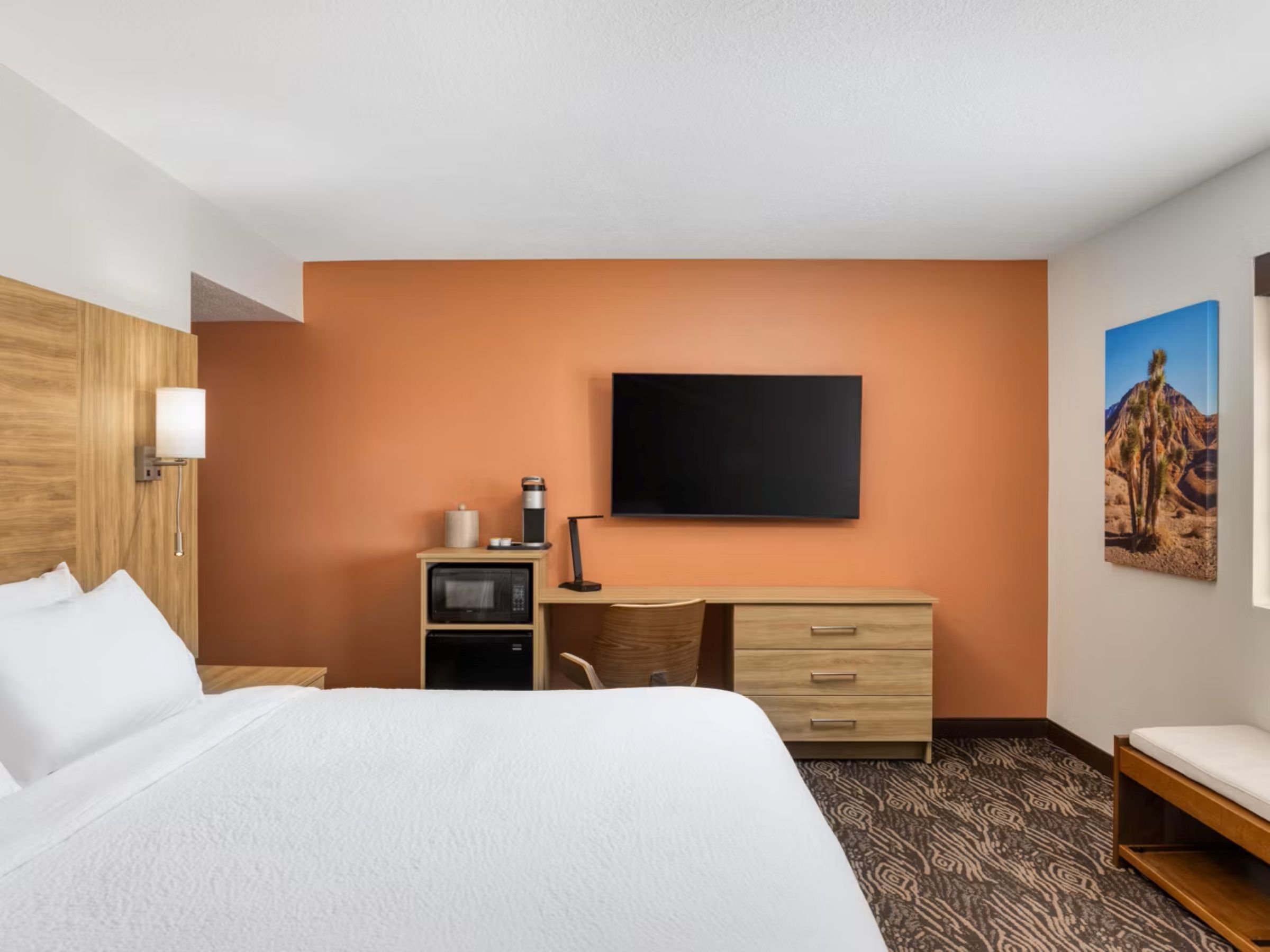 A hotel room with a bed, desk, chair, and a flat-screen TV mounted on the wall.