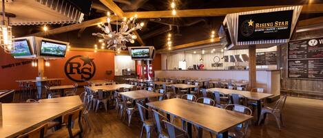 A spacious restaurant with multiple tables and chairs, a bar area, and a large screen displaying sports.