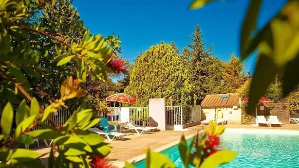 Una piscina con sillones de descanso y un paraguas rojo, rodeada de vegetación y árboles.