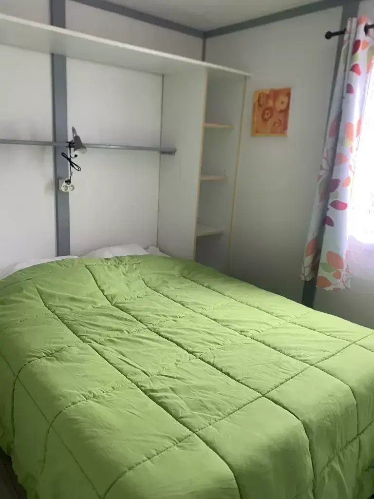 Habitación con una cama individual, una colcha verde, un cabecero blanco y un estante en la pared.
