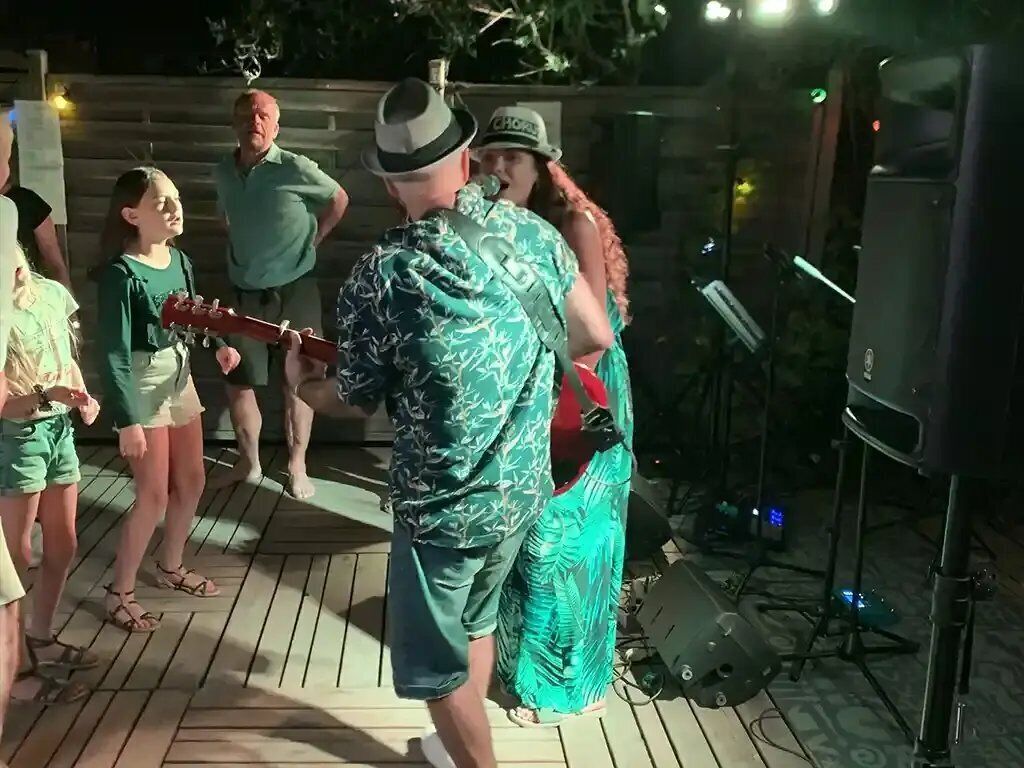 A group of people on a wooden deck with musical equipment, including a guitar and speakers.