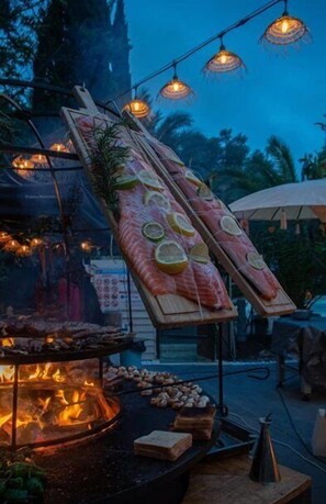 A seafood display with grilled items and a fire pit, set against a backdrop of trees and string lights. - ZEcamping 3* piscine animaux acceptés mobil-home LV 6 pers (Tuchan)