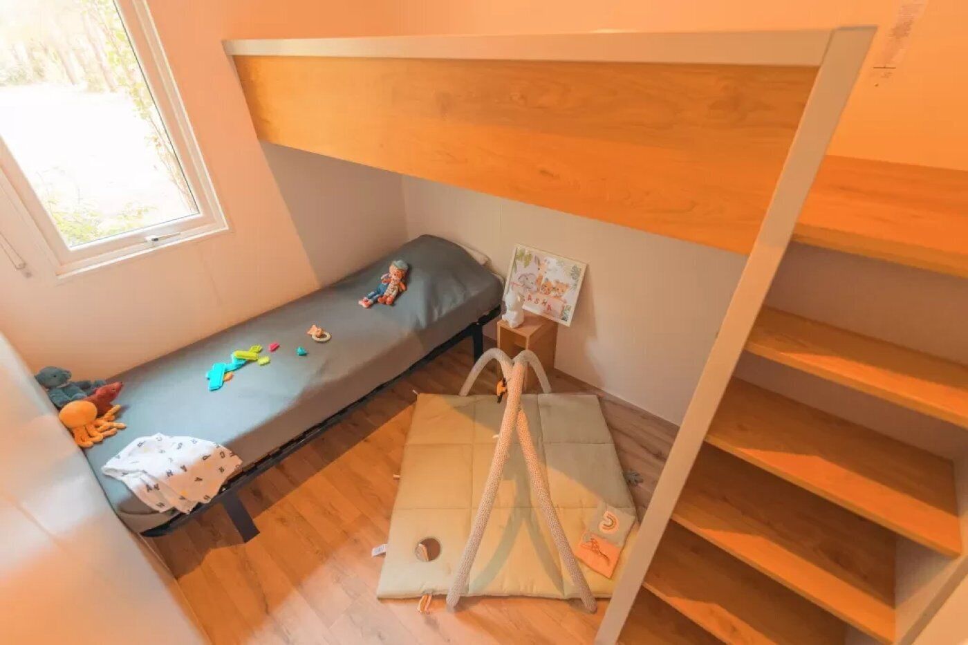 Een kleine, knusse kamer met een stapelbed, een enkel bed en een raam.